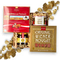 Geöffnete Geschenkbox gefüllt mit Heindl Spezialitäten, Wiener Nougat, einer Dose Reber Mozartkugeln, Bergland-Honig und einem Holzlöffel.
