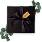 Hochwertige, geschlossene Geschenkbox aus geriffeltem schwarzem Premiumkarton, elegant gebunden mit einer schwarzen Satinschleife und einem geschenkify-Anhänger.