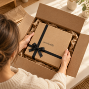 Frau packt eine geschenkify Geschenkbox mit schwarzer Schleife aus dem Versandkarton aus, sicherer Geschenkversand